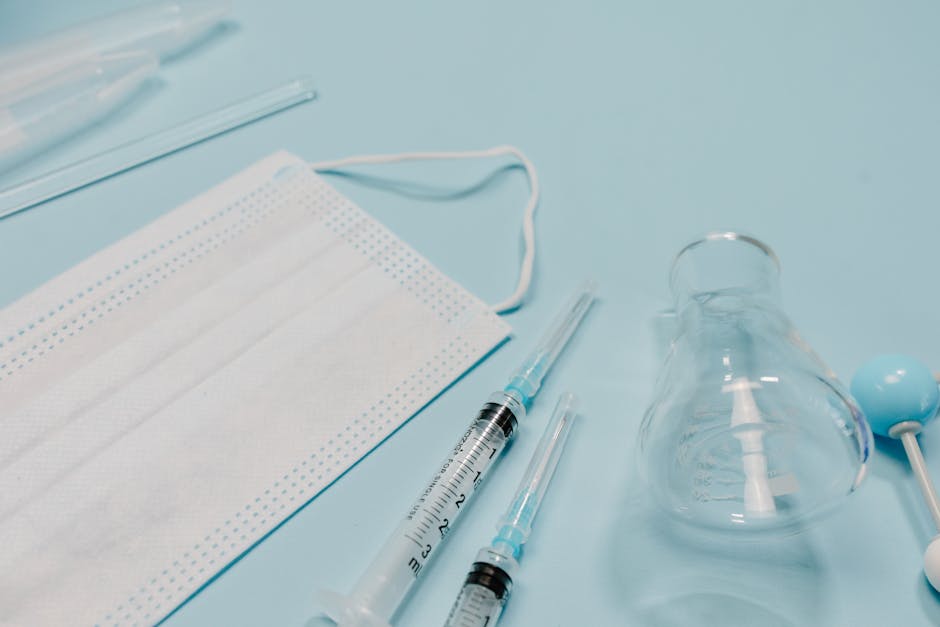 The image displays a medical-themed scene with two transparent plastic syringes, each fitted with a blue needle cap, positioned parallel to each other on a light blue surface. To the right of the syri